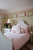 Bed with curved headboard and pink bed linen against light grey wooden wall