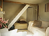 Plain living room with throw and fur-covered cushion on sofa and ottoman beneath staircase