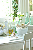 Knoblauch im Mörser, Olivenöl und Besteck am Küchenfenster