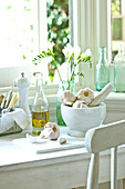 Garlic in a mortar, olive oil and cutlery in front of a kitchen window