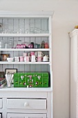 Glasses, cups and painted wooden case on white-painted kitchen dresser