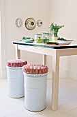 White metal stools with cushions next to kitchen table with still-life arrangement in corner of minimalist room with baking tins on wall