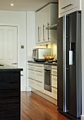 Corner of designer kitchen with white cupboard doors and stainless steel, upright fridge