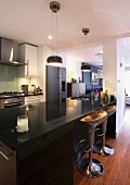 Designer kitchen counter with glossy black work surface and bar stools in open-plan kitchen