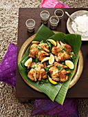 A spring chicken with coriander and lemon wedges on a banana leaf
