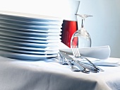 Stacked porcelain plates, linen napkins, cutlery and glasses on table