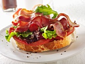 A slice of baguette topped with bacon, lettuce and tomato