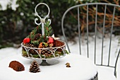 Metal cake stand with natural decorations and baubles on snowy garden table
