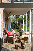 Rustic wooden chairs with colourful cushions and furs on a covered wooden terrace with antique steel chairs