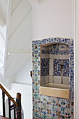 A hallway with an antique coloured wooden banister and an old wash basin in a wall niche with historic Delft tiles