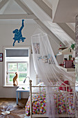 A wrought iron bed with a colourful bedspread and a mosquito net in a child's bedroom with a blue monkey cut out of wall paper above the window