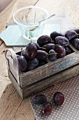 Fresh plums in a wooden crate with an empty glass bowl next to it