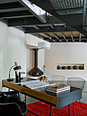 Retro desk with wire-framed chairs in minimalist living area with gallery and exposed steel structure