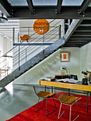 60s-style desk and chairs in open-plan interior below gallery with steel staircase