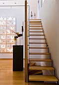 Treppe mit Holzstufen in offenem Vorraum und Kunstobjekte auf Stele und an der Wand