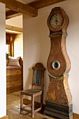 Antique grandfather clock with curved case and an old wooden chair in a renovated, rustic old building