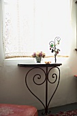 Small, old console table with metal legs in stylized heart form under a window with a romantic retro curtain