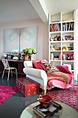 XXXL-Sessel vor Bücherregal und moderne Kunst über altem Schreibtisch - Wohnraum mit rot und rosafarbenen Teppichen und Accessoires