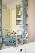 Bathtub fitting in retrostyle in front of an antique mirror with carved, blue pastel frame