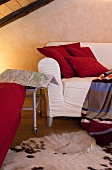 White sofa below wooden ceiling with red cushions and striped, woollen blanket; animal skin rug provides a cosy atmosphere