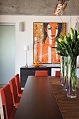 Long dining table with a purple bouquets in glass vases and modern art on the wall
