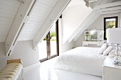 Weisses Schlafzimmer mit eleganten Möbeln im Antikstil unter der sichtbaren Dachkonstruktion eines modernen Landhauses