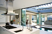 A white kitchen counter with an extractor fan and a view over an open courtyard with a pool and an adjoining living room-cum-dining room