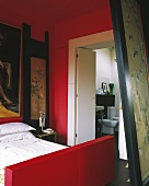 Bed with red bedstead in red-painted bedroom with ensuite bathroom