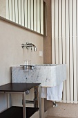 Modern stone sink with wall-mounted taps and side table in corner of bathroom