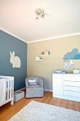 Weiß blau getöntes Kinderzimmer mit gemaltem Hasenmotiv an Wand und Sessel neben Kommode