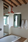 Designer bathroom with red lacquered chandelier hanging from wooden beams of ceiling in renovated country house