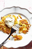 Potato rösti (hash brown) with sour cream on a plate with a fork