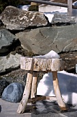 Rustic wooden footstool in front of boulders and a small snow shovel