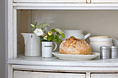 Bread in dish amongst crockery on dresser surface