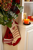 Knitted Christmas stockings hanging below flower arrangement with roses and hydrangeas and next to lit candle on living room cabinet