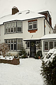 Eingangsseite eines zweistöckigen Wohnhauses im Winter mit Schnee auf Dächern und Weg
