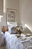 Verschiedene Bilderrahmen und ein Teddybär auf der Tagesdecke eines Holzbettes