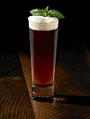 Tall Glass of Amber Beer with a Basil Garnish