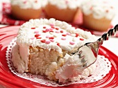 Kleiner herzförmiger Kuchen mit weißem Zuckerguss und Zuckerherzen