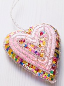 A fabric heart decorated with sequins on a white surface