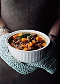 A woman holding a bowl of beef and carrot stew