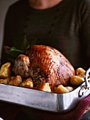 A woman a turkey and roast potatoes in a roasting tin
