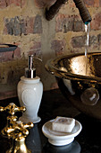 Water running into brass sink on washstand against brick wall
