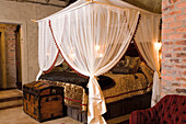 Four-poster bed with canopy and shiny gold bedspread in bedroom with exposed brick walls