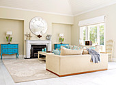 Pair of pastel blue, antique chests of drawers either side of open fireplace in traditional living room with two large couches