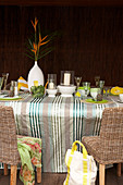Decorated table with candles and glass candle covers on a striped table cloth in front of a dark wood wall