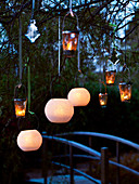 Various candlelit lanterns hanging on tree and view across bridge in background