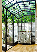 Conservatory with dark metal frame construciton, an antique chest of drawers and parquet flooring