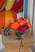 Bouquet of pink and orange roses on designer stool; cushions and bedspread in matching colours in background