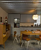 Modern, retro chairs and simple wooden table in open-plan kitchen with fifties charm